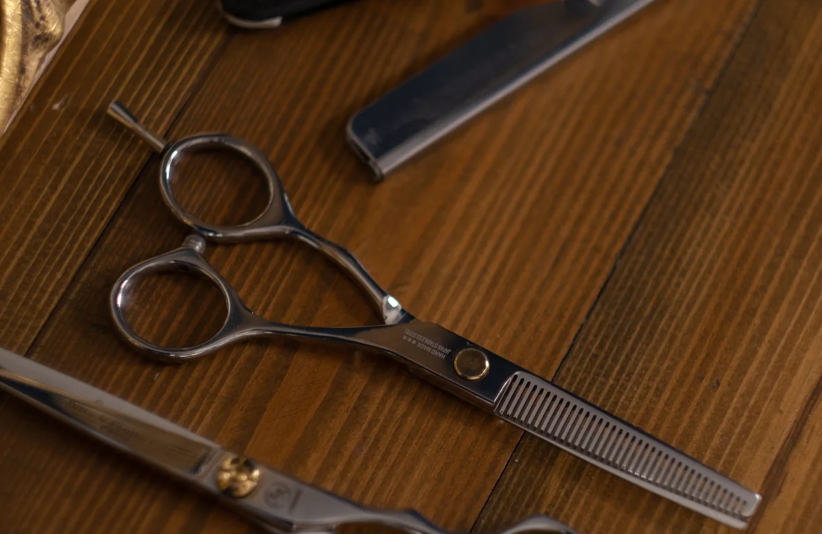 Traditional barber scissors and straight razor arranged on wood, used as the preview for the editorial barbershop template